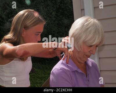 Petite-fille de 12 ans qui tond les poils des grands-mères pendant le shutdown Covid-19. La grand-mère est patiemment assise par la procédure. Banque D'Images