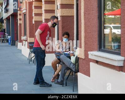 Oak Park, Illinois, États-Unis. 17 juin 2020. Un serveur sert les clients dans un café-terrasse. Les restaurants de la région de Chicago sont désormais ouverts pour des places assises à l'extérieur avec une distance sociale appropriée. Les serveurs doivent porter des masques. Le taux d'infection par le virus COVID-19 de l'Illinois diminue plus rapidement que dans les autres États en raison de l'état de vie vigoureux à la maison et des directives de distanciation sociale. Banque D'Images