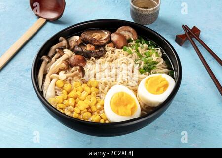 Rampe. Nouilles soba avec œufs, champignons et légumes, avec saké, cuillère en bois traditionnelle et baguettes, sur un backgro bleu Banque D'Images