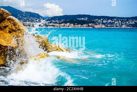 Vagues de l'océan de la Méditerranée qui s'écrasant et éclaboussant sur des rochers. L'eau est une belle couleur turquoise. Prise à Nice, France. Banque D'Images