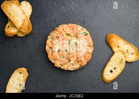 Tartare de saumon vue de dessus, un plat fait avec du saumon frais haché, de l'avocat, de la sauce tartare et des craquelins ou du pain. Plat de hors-d'œuvre sain. Banque D'Images