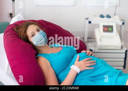 Patiente enceinte sous masque facial à l'hôpital lors de la visite d'un médecin pendant l'éclosion du coronavirus. Mère donnant naissance à bébé en covid-19 verrouillage. Grossesse e Banque D'Images