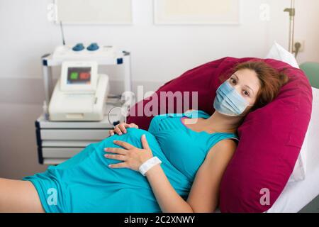 Patiente enceinte sous masque facial à l'hôpital lors de la visite d'un médecin pendant l'éclosion du coronavirus. Mère donnant naissance à bébé en covid-19 verrouillage. Grossesse e Banque D'Images