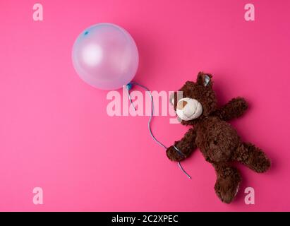 Petit ours en peluche brun tenant un ballon bleu sur une corde sur un fond rose Banque D'Images