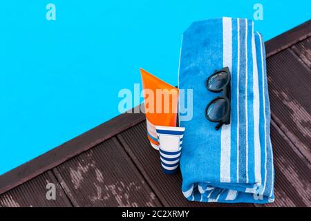 lunettes de soleil, tube de crème solaire, serviette bleue près de la piscine, fond tropical Banque D'Images