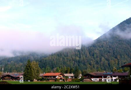paysage avec fermes en premier plan et montagne boisée derrière avec brouillard et ciel bleu Banque D'Images