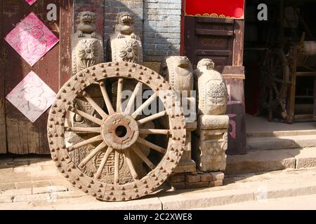 Image montrant une roue en bois cloutée en métal antique et quelques sculptures et meubles devant un magasin d'antiquités, Zhou Cun, province de Shandong, Chine Banque D'Images