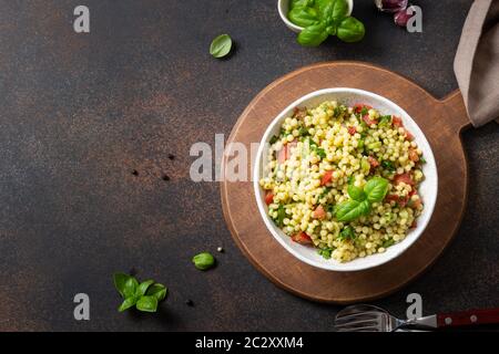 Salade de légumes avec pâtes ptitim ou Birdy, feuilles de basilic à la décoration israélienne couscous sur fond noir. Vue de dessus. Banque D'Images