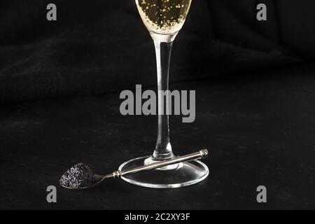 Black caviar sur une cuillère, un verre de champagne, sur un fond noir avec une place pour le texte Banque D'Images
