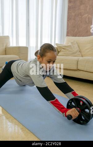 Petite fille faisant du sport dans le salon à la maison sur un tapis bleu Banque D'Images