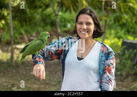 La femme pose avec un sourire comme elle porte son bras à une macaw dans un camp Banque D'Images