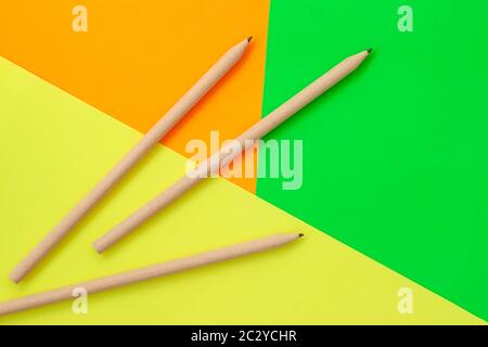 Trois crayons simples sur fond multicolore lumineux, pose plate. Retour à l'école et concept d'éducation Banque D'Images