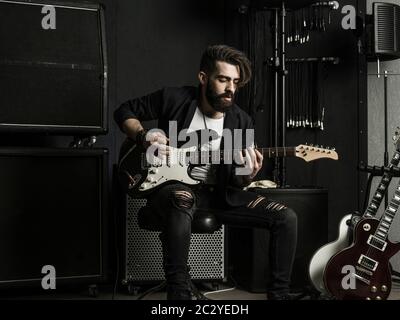 Photo d'un homme à barbe assis et jouant de sa guitare électrique dans un studio d'enregistrement. Banque D'Images