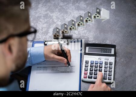 Homme Calculant La Facture Devant Les Modèles De Maison Sur L'Escalier Flèche Croissante Banque D'Images