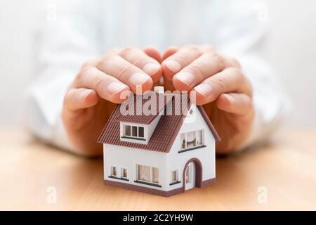Assurance de biens. Maison miniature couverte par les mains Banque D'Images