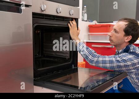 Jeune homme technicien dans la vérification de l'ensemble four dans la cuisine Banque D'Images