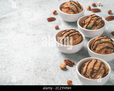 Pâte à biscuits brute de monstre sans danger à manger dans un petit bol de portion et noix sur fond de ciment gris. Idées et recettes pour les repas pour enfants et enfants en bas âge. Copier la flèche Banque D'Images