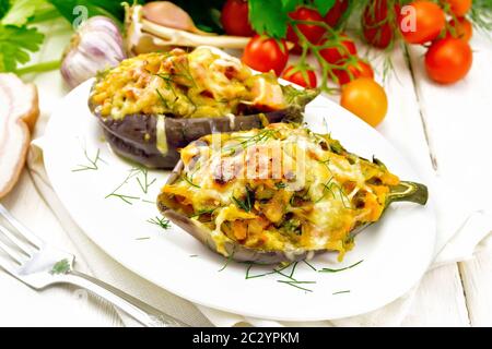 Aubergines farcies avec poitrine fumé, tomates, oignons, carottes à l'ail, le fromage et les herbes dans une assiette sur une serviette sur fond blanc bois Banque D'Images