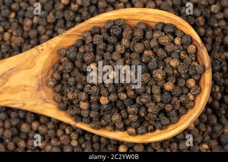 Fond d'épices, fond fait de beaucoup de grains entiers de poivre noir et une cuillère de cuisson faite de bois d'olive également rempli de poivre , très proche Banque D'Images