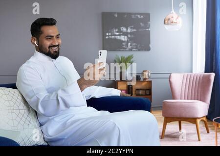 Un homme saoudien visiophonie à la maison assis sur un canapé dans le salon Banque D'Images