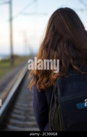 Une fille marche sur des rails de chemin de fer dans un manteau - voyage, dépression, style de vie Banque D'Images