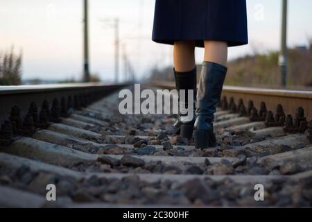 Une fille marche sur des rails de chemin de fer dans un manteau et des bottes - Voyage, dépression, style de vie Banque D'Images