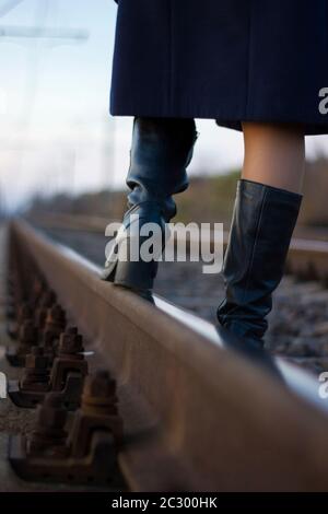 Une fille marche sur des rails de chemin de fer dans un manteau et des bottes - Voyage, dépression, style de vie Banque D'Images