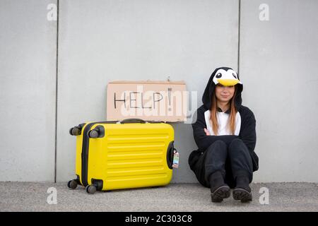 Jeune femme, avec le costume de pingouin et valise jaune, doit voyager en raison du réchauffement climatique. Triste symbole d'un manchot qui doit quitter sa patrie bec Banque D'Images