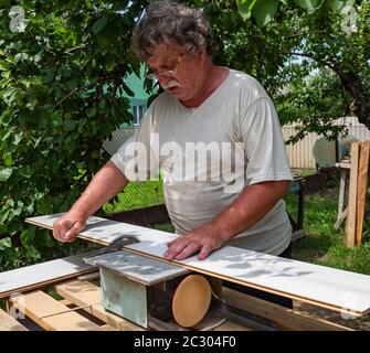 Homme de race blanche utilisant une scie circulaire pour couper la planche de parquet dans le jardin Banque D'Images