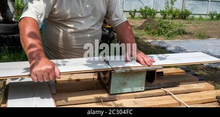 Homme de race blanche utilisant une scie circulaire pour couper la planche de parquet dans le jardin Banque D'Images