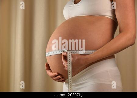 Vue de profil rapprochée de la femme enceinte caucasienne qui vérifie son ventre exposé avec une bande de mesure, vue de bas angle Banque D'Images