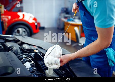 Un employé en uniforme vérifie le niveau d'huile moteur, poste d'entretien de voiture. Contrôle et inspection automobiles, diagnostic et réparation professionnels Banque D'Images