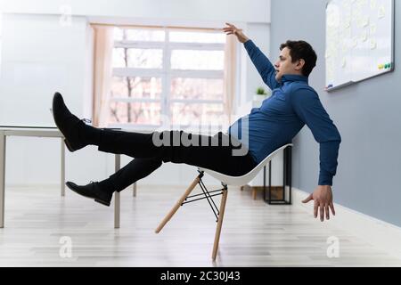 Photo De L'Homme Tombant Sur La Chaise Au Bureau Banque D'Images