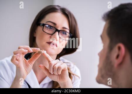 Jeune femme médecin montrant à l'aide auditive Male Patient In Clinic Banque D'Images