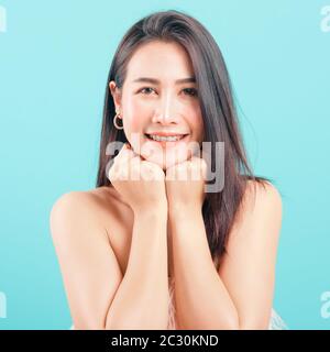 Visage souriant Asian belle femme sa heureuse garde les deux mains sous les sourires de menton agréablement sur fond bleu Banque D'Images