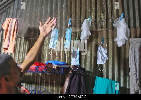 Un homme qui pendait des masques et des gants de main sur une corde après les avoir lavées pour être utilisé à nouveau pendant la pandémie du coronavirus à Korail slum.la plus grande taupe de la capitale Dhaka, Korail compte près de cinquante mille habitants qui ne connaissent pas la maladie mortelle. Les bidonvilles présentent un grand risque pour la santé de résultats extrêmes, car les endroits bondés sont très sensibles à l'épidémie de Covid-19. Banque D'Images