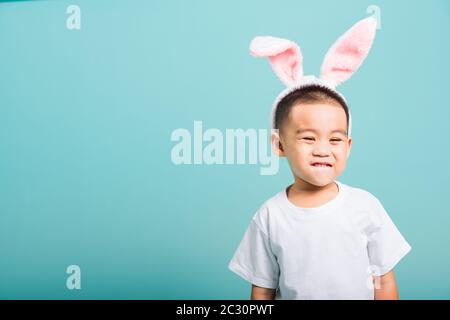 Concept du jour de Pâques, Joyeux asiatique mignon petit garçon sourire beaming portant des oreilles de lapin et un T-shirt blanc debout sur fond bleu avec espace de copie Banque D'Images