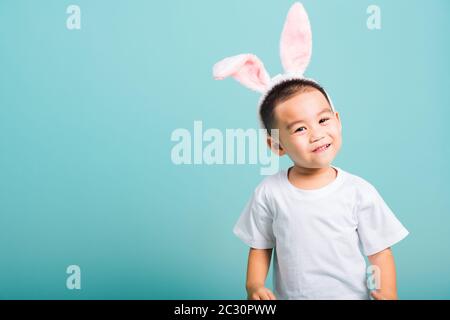 Concept du jour de Pâques, Joyeux asiatique mignon petit garçon sourire beaming portant des oreilles de lapin et un T-shirt blanc debout sur fond bleu avec espace de copie Banque D'Images