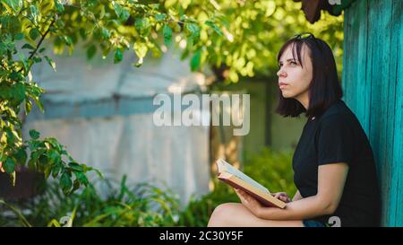 Gros plan de la jeune femme avec livre dans le jardin. Femme se reposant dans la nature, appréciant son temps libre. Banque D'Images