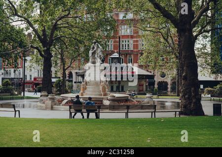 Londres, Royaume-Uni - 13 juin 2020 : peu de personnes se détendent sur un banc devant une fontaine à Leicester Square, l'une des plus populaires et typiquement très bu Banque D'Images