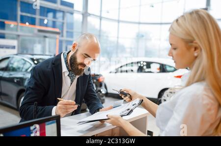 Man signe un contrat pour acheter une nouvelle voiture dans un concessionnaire de voiture. Client et vendeur dans la salle d'exposition de véhicules, homme achetant le transport, concessionnaire automobile Banque D'Images