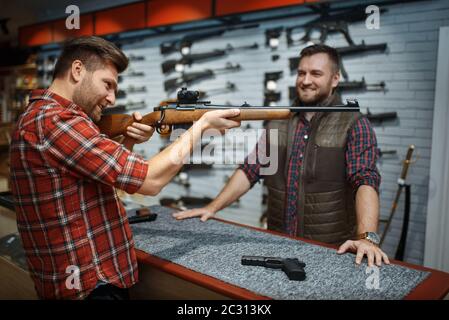 Man vise avec un nouveau fusil, vendeur au comptoir dans la boutique d'armes à feu. Homme personne achetant une arme en magasin, chasse et sport de tir hobby Banque D'Images