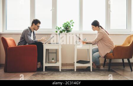 Vue latérale photo d'un couple d'affaires caucasien travaillant de la maison à l'ordinateur et écrivant quelque chose près de la fenêtre Banque D'Images