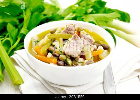 Eintopf soupe de porc, le céleri, les haricots, les carottes et les pommes de terre avec le poireau dans un bol blanc sur une serviette sur planche de bois contexte Banque D'Images