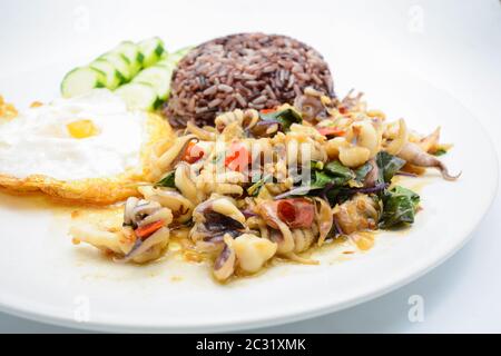 Calmar épicé sauté aux feuilles de basilic et au piment, œuf Sunny, servi avec du riz brun. C'est le cas Banque D'Images