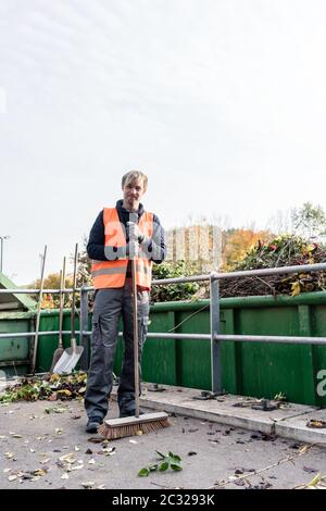 Homme balayant le sol du centre de recyclage après avoir placé le vert de déchets dans le conteneur Banque D'Images