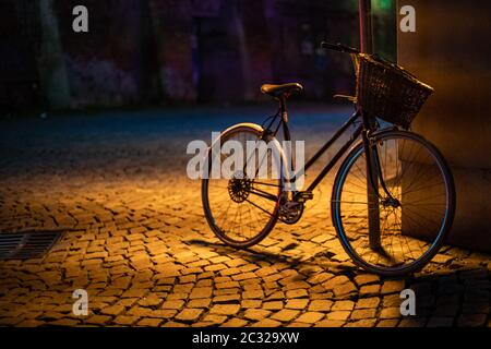 vélo rétro écrasé à un poteau sur une rue de ville, éclairé par une lampe la nuit Banque D'Images