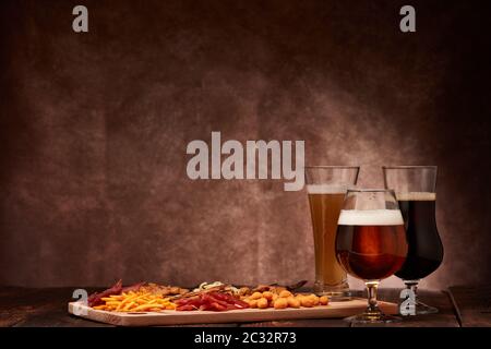 Trois verres avec différentes bières et un ensemble de divers en-cas : jerky, chips de pommes de terre, noix salées, poisson à rupture, biscuits épicés au pain, calmars séchés Banque D'Images