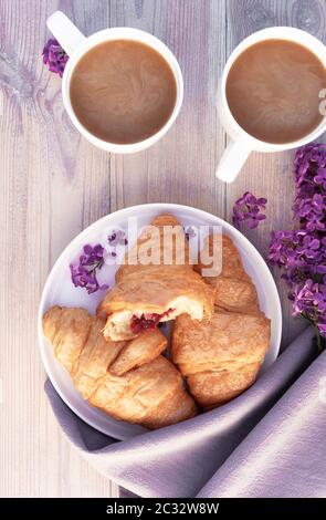 Deux belles tasses de café en porcelaine avec du lait et des croissants décorés de fleurs lilas sur une table en bois blanc. Concept de petit déjeuner parfait. Plat l Banque D'Images