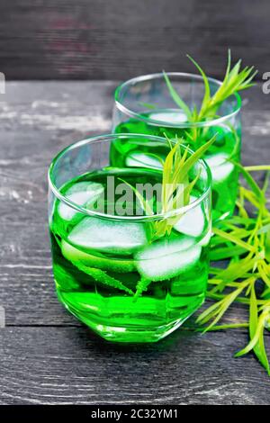 Limonade d'estragon dans deux verres avec glace, plates-formes d'estragon sur fond de planche en bois noir Banque D'Images